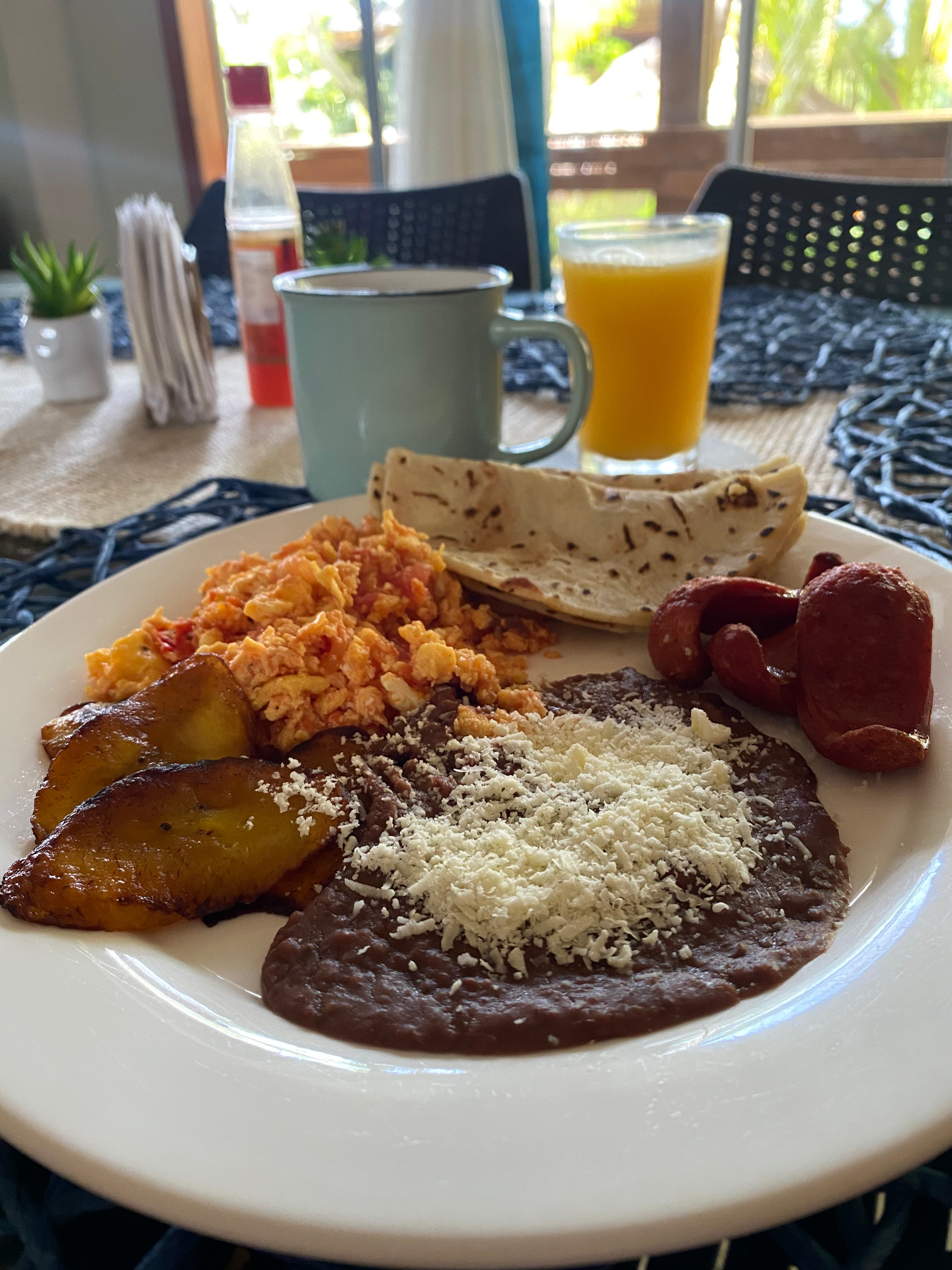 Honduran breakfast plate with refried beans, cotija cheese, sweet plantains, scrambled eggs with tomato, fried sausage and tortillas